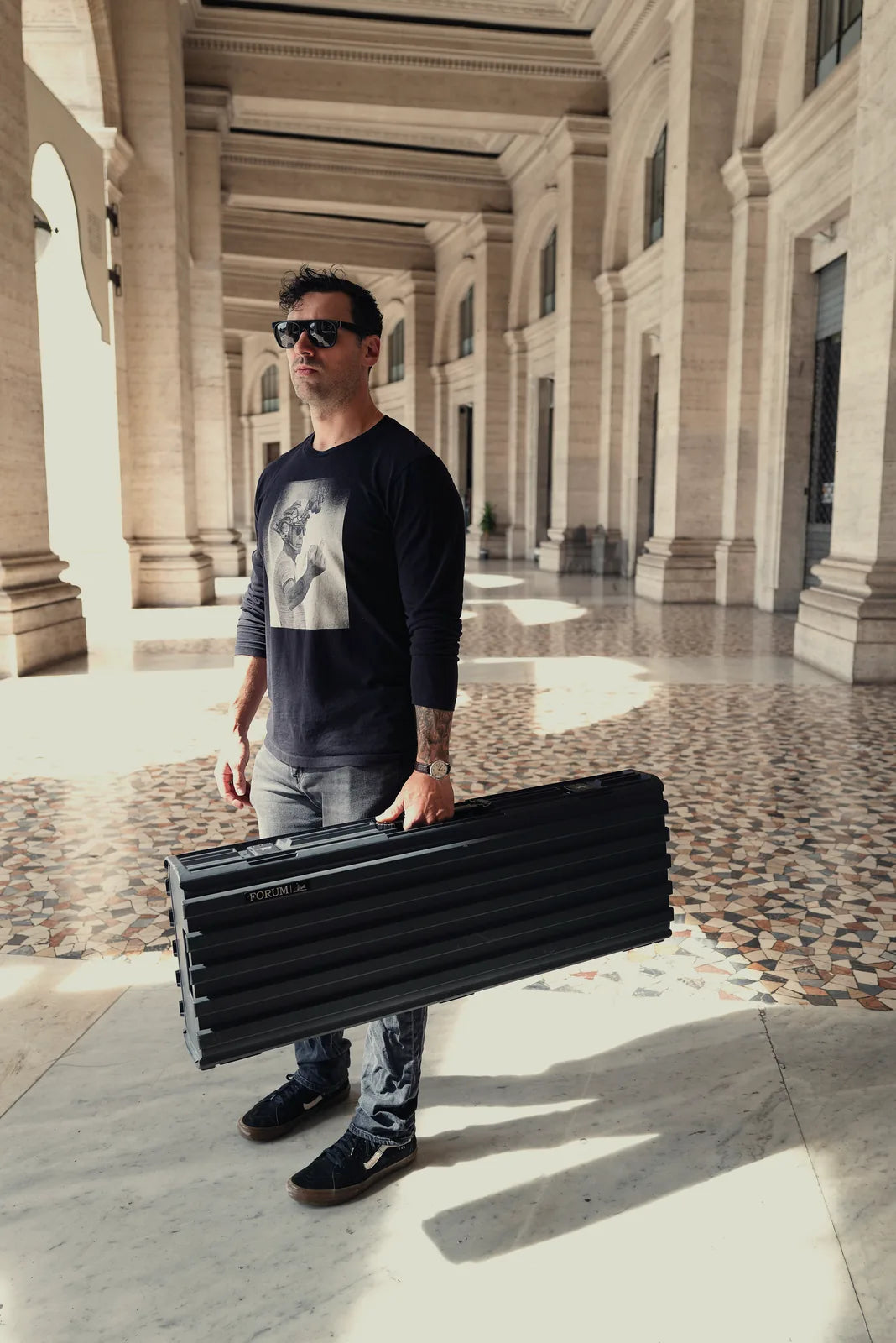 A man holds the Theseus case under a Roman colonnade