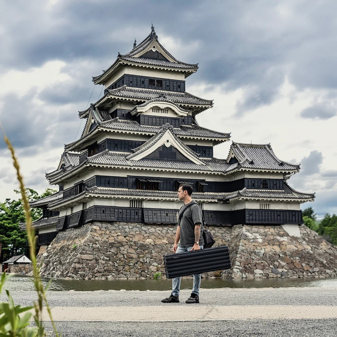 A man stands with the Theseus case before a black Japanese castle